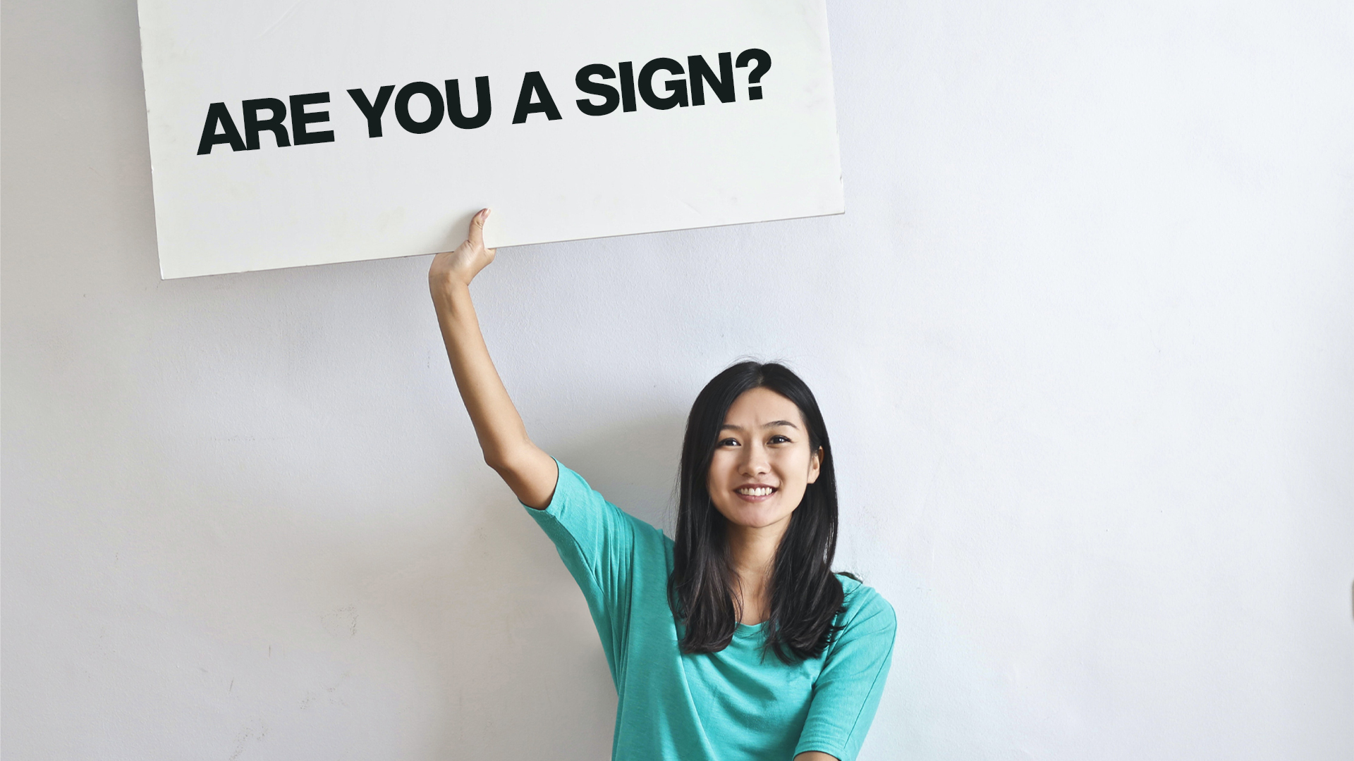 A lady holding up a large piece of card which reads: 'are you a sign?'