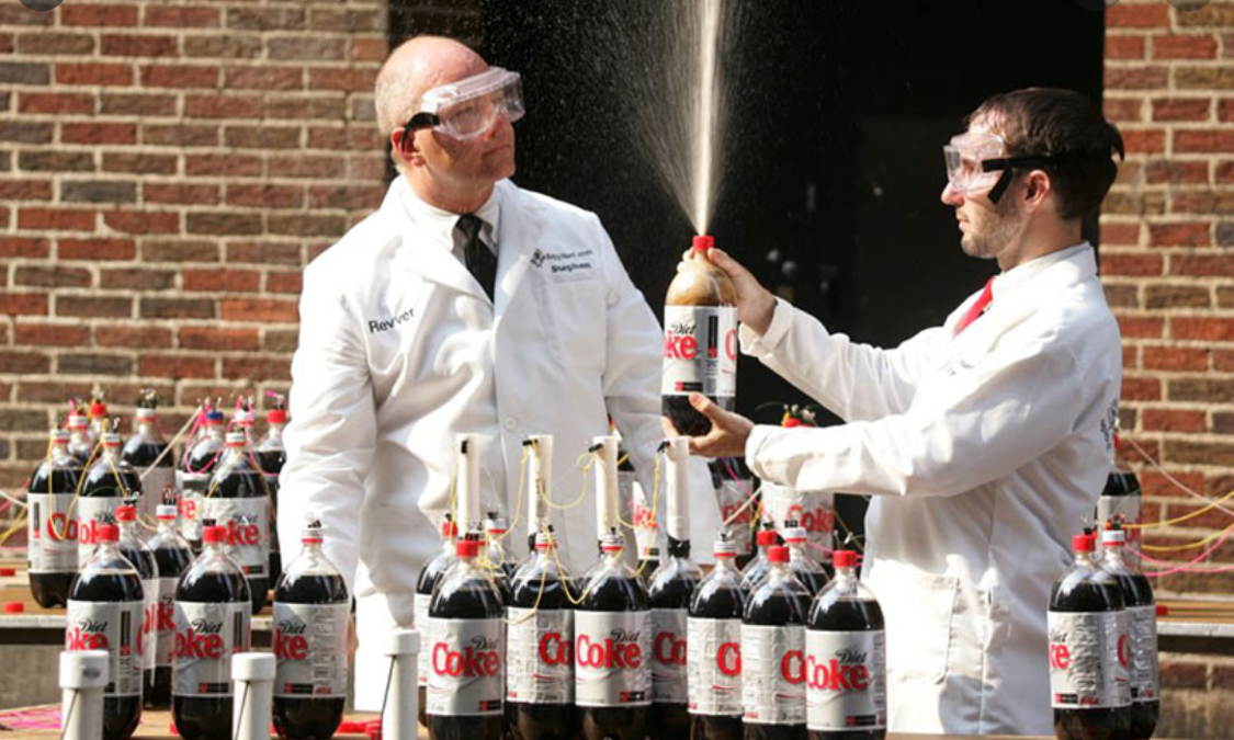 Two scientists doing the Mentos experiment on many bottles of Coca Cola