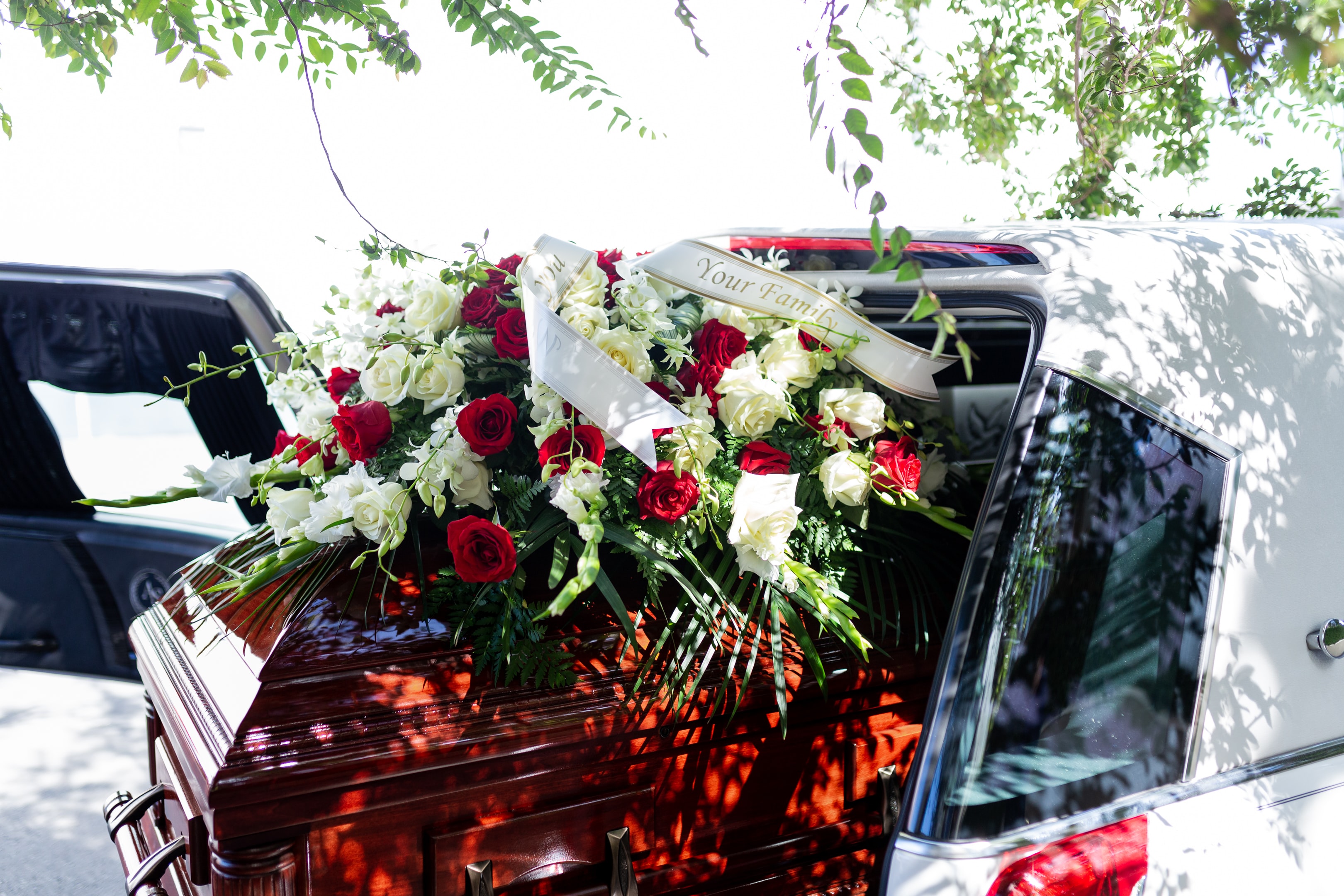 A hearse with a coffin partially in. The coffin is covered with red and white roses