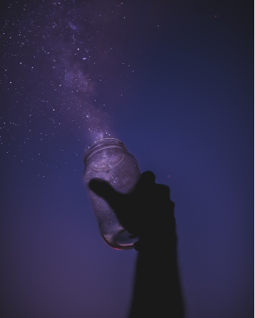 A hand pointing to the sky holding a jar. The jar appears to be releasing stars back to the the night sky