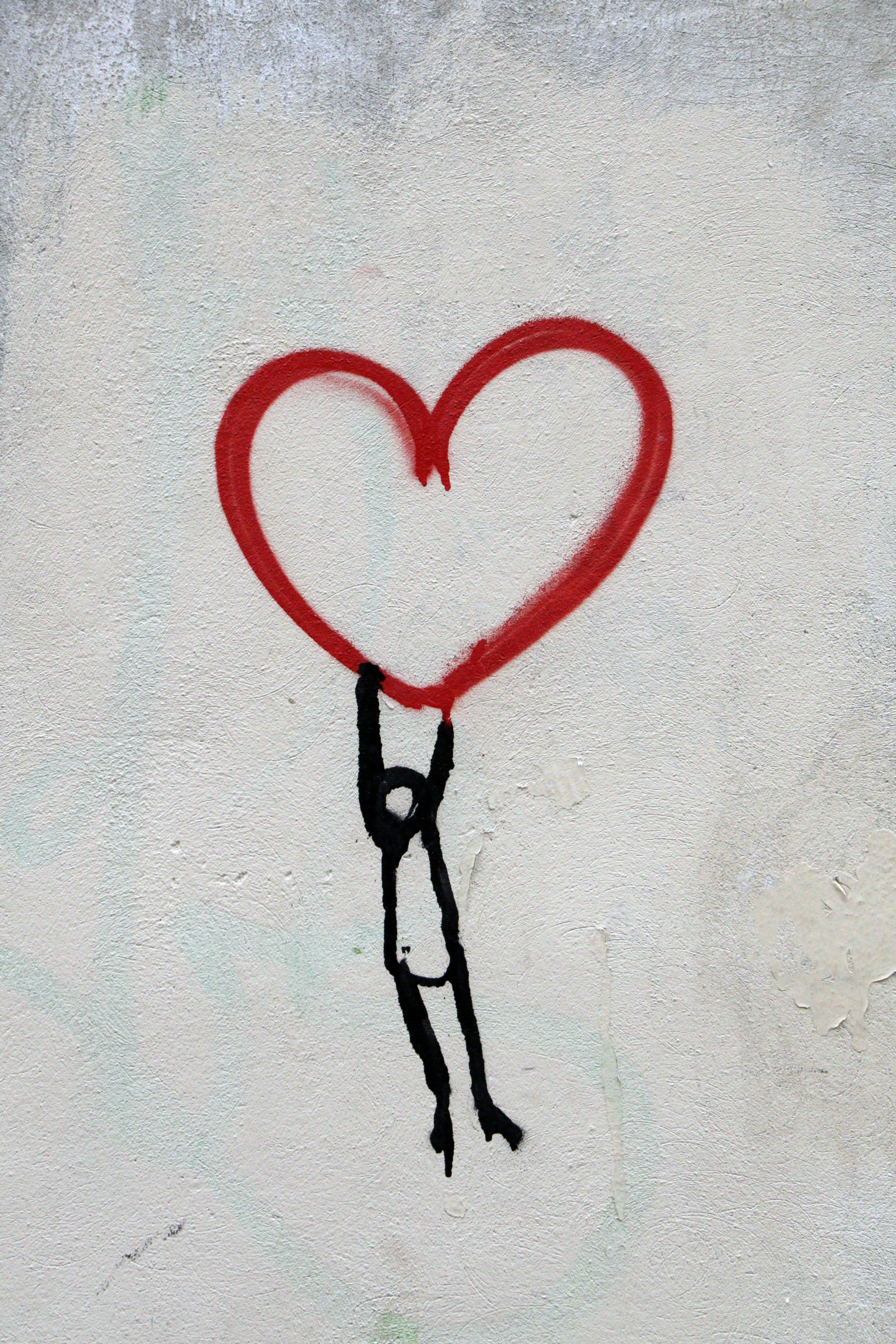 A drawing of a red heart with a stick person hanging on to the bottom of the heart