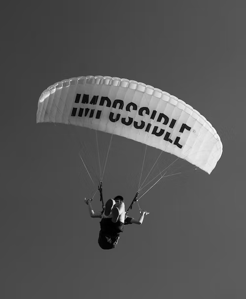 A person parachuting. The parachute is the wing type and has the word 'Impossible' on it