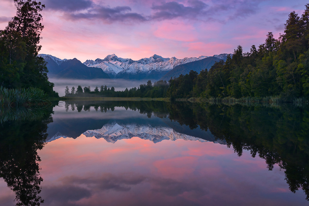 A view over a lake to the mountains and forest. There is a perfect mirror image in the lake.