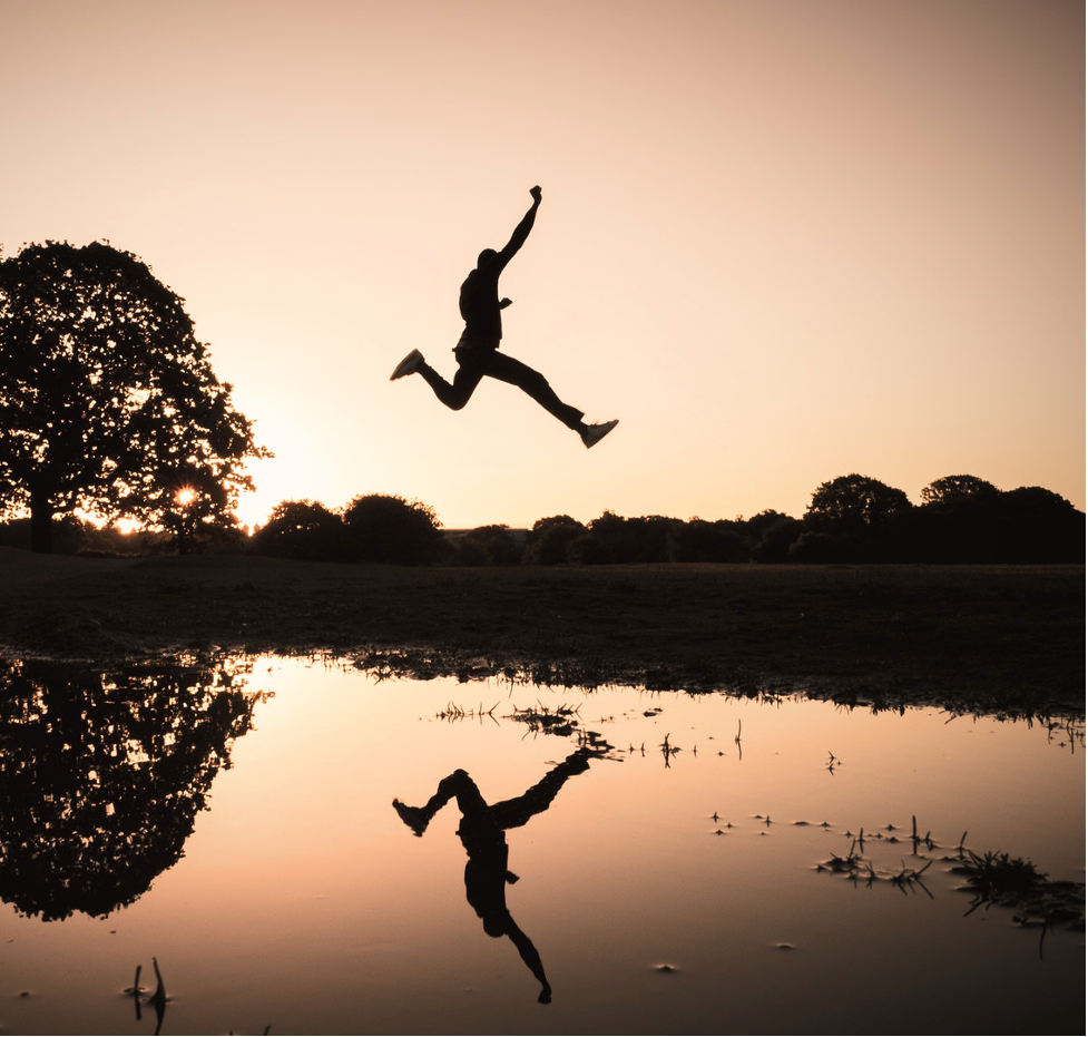 A silhouette of a person jumping over the river