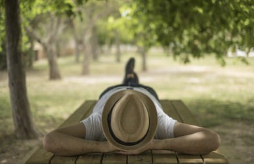 A man with a hat lying on a picnic table in the trees