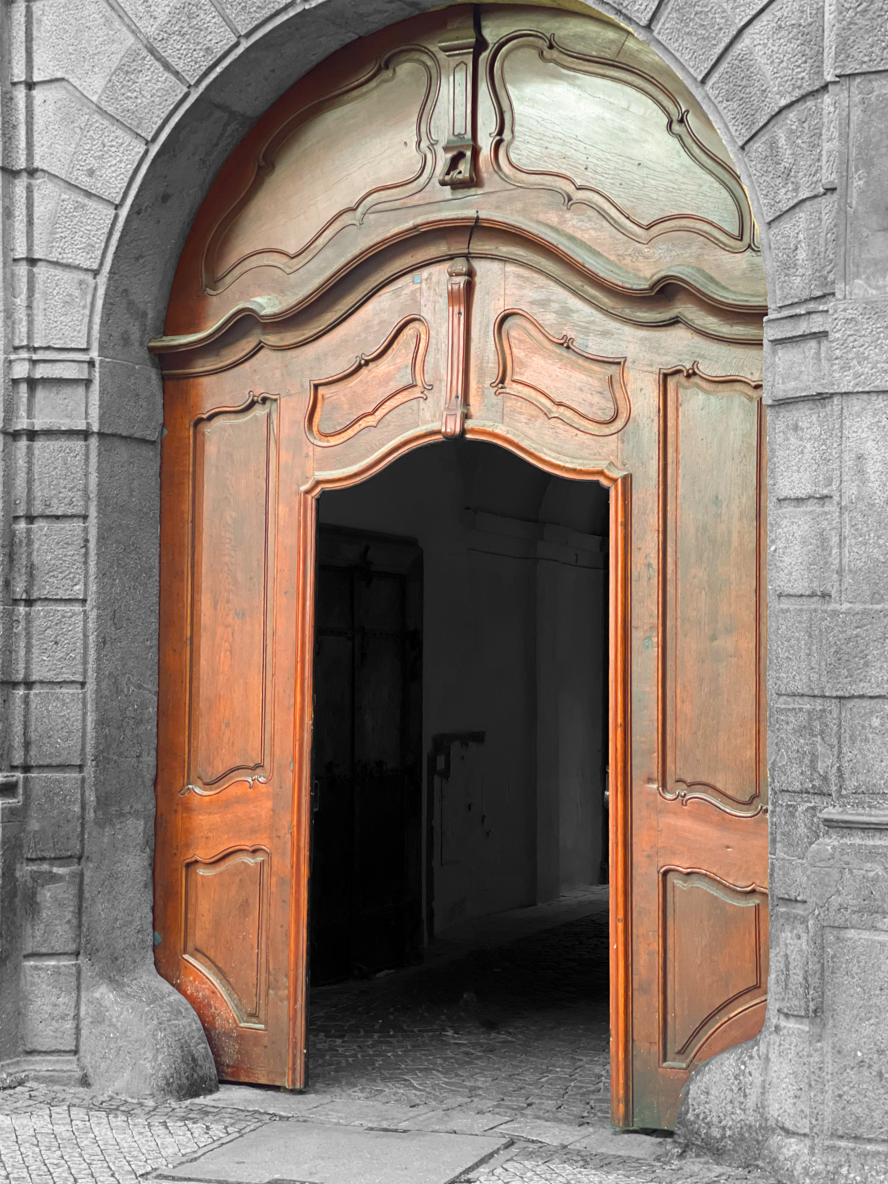 An ornate arched wooden door with a stone surround. The wooden door is open.