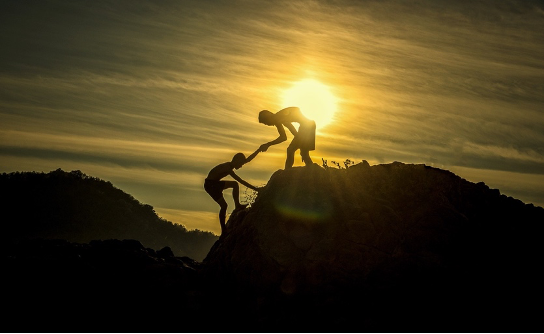A silhouette of a climber helping another climber up a rock