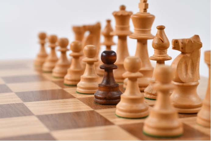 Close up of a chess board with white chess pieces. There is one brown pawn.