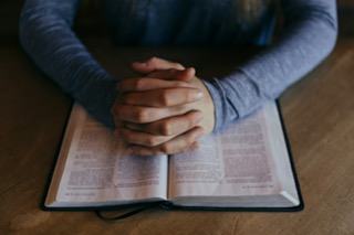 Open bible with hands clasped in prayer over the top