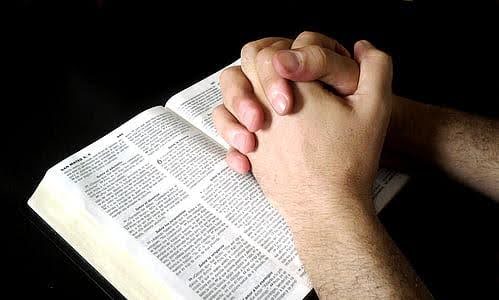 Open bible with a set of hands in a clasped prayer position