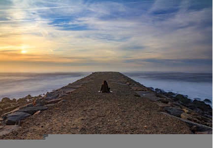 A straight stone jetty leading out to sea. A person is sat on the jetty.