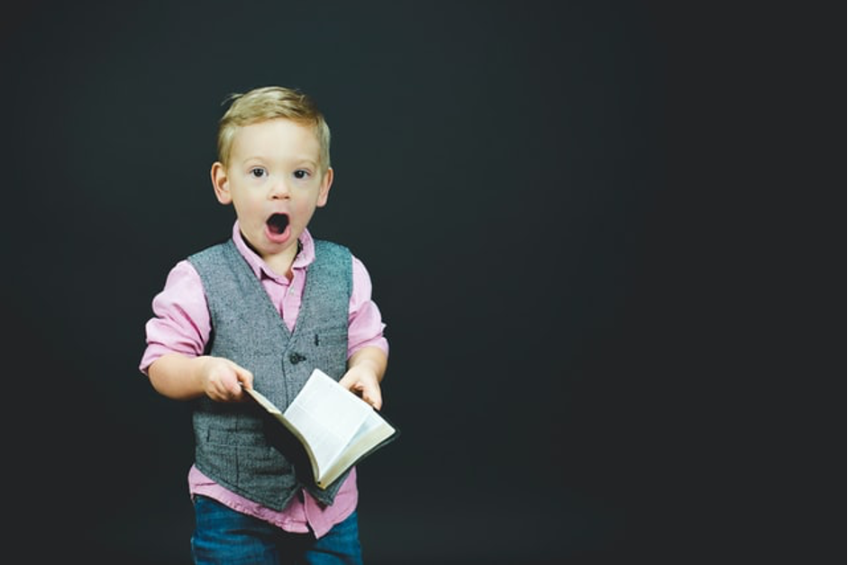 A child holding a book with a shocked expression on his face